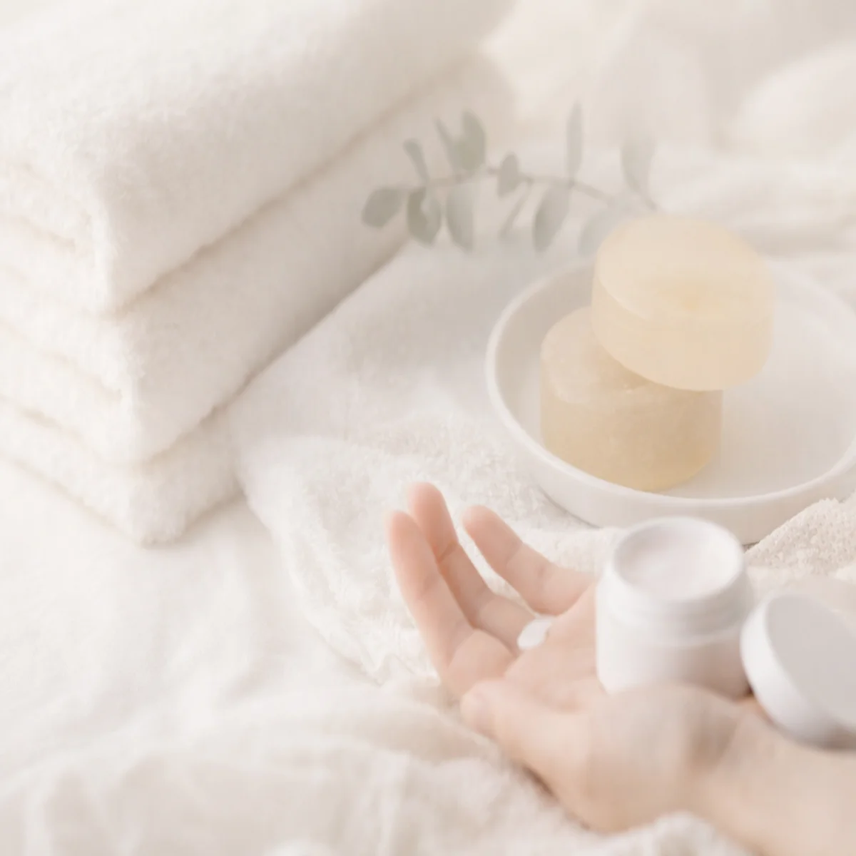 白いタオルと石鹸が置かれた静かなケアシーン。手のひらにクリームをのせて整えるやさしい夜のイメージ。